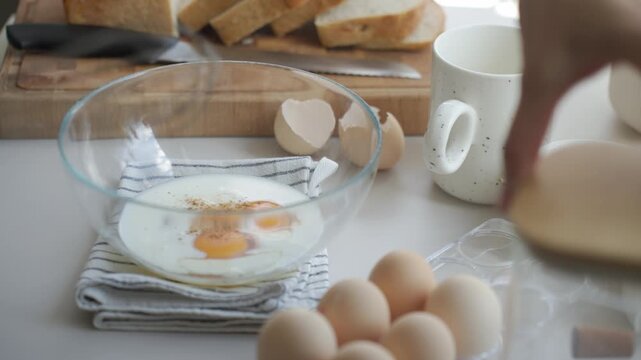 Hand adds salt to egg mixture in bowl before whisking, with bread slices nearby