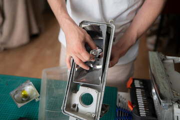 Individual is focused on fixing a car light at a work table filled with tools and parts in a workshop © Mihail