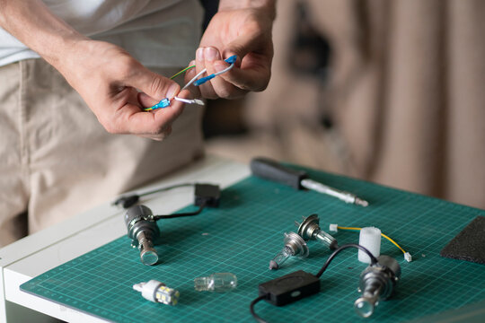 Hands connect wires while working on electrical parts at a table with tools and components in view