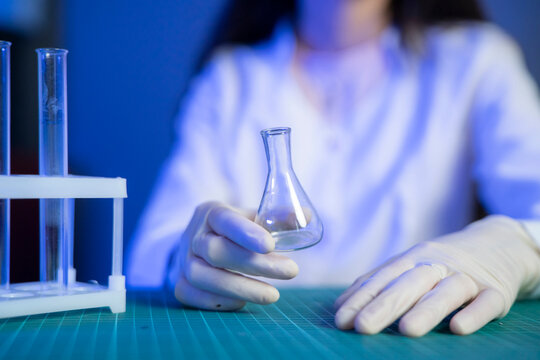 A scientist in a lab coat holds a glass flask while working at a table with test tubes nearby