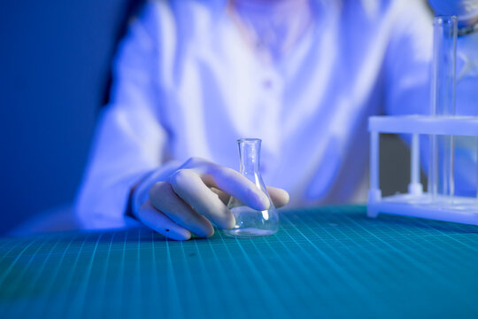 A scientist in a lab coat works with a glass flask and equipment while studying vaccine formulation at night