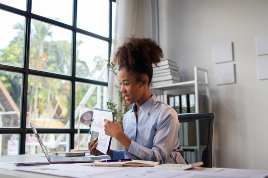 Confident businesswoman in a modern office, participating in a virtual meeting and reviewing financial reports during a video conference call.