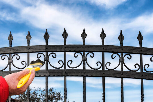 Hand Painting a Metal Fence with a Brush. Home Maintenance, Rust Protection, Renovation, and DIY Improvement Concept.
