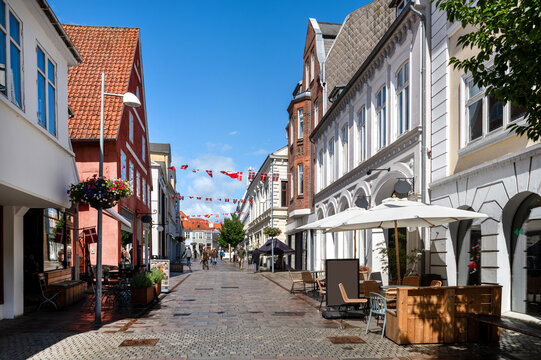 Pedestrian street with historic facades, caf&eacute;s, Danish flags and a blue summer sky in the center of Sonderborg, Denmark