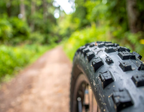 Close-up of a knobby mountain bike tire on a dirt trail, focus on rugged rubber tread patterns, cycling equipment on a forest path, outdoor adventure travel.