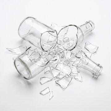 Broken glass bottles lie in a chaotic pile on a white surface creating a sharp and dangerous mess for the viewer.