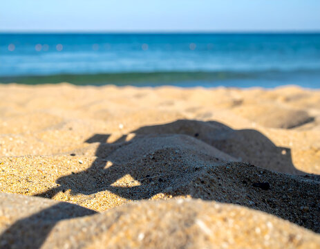 Shadow of a person holding a phone on sandy beach with ocean waves. Close up of golden sand textures, bright summer sunlight, coastal leisure and vacation.