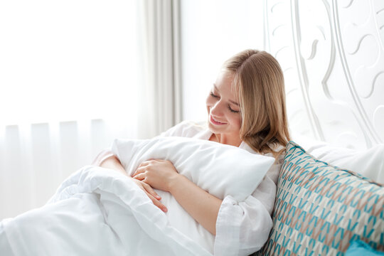 Young woman relaxing in bed, hugging pillow. Self-care, home wellness and cozy lifestyle. Mindful morning routine, slow living