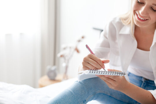 Young woman writing in journal, drawing. Girl relaxing in bed. Art therapy, self-care, female wellness. Mindful morning routine in cozy home. Slow living, analog lifestyle, digital detox. Close up