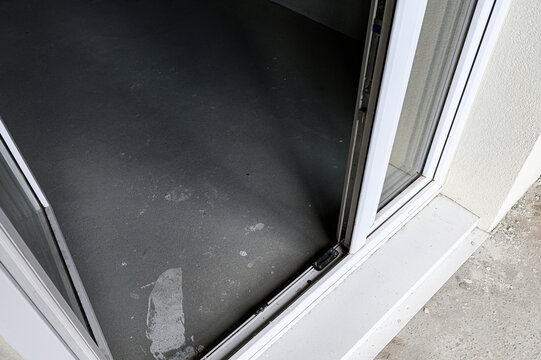 white PVC balcony door features dark threshold with minor surface wear. frame aligns with beige wall and concrete floor, highlighting threshold‑free transition