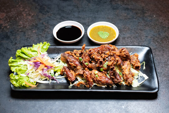 Deep fried pork intestines served with fresh side salad on a black rectangular plate over dark background.