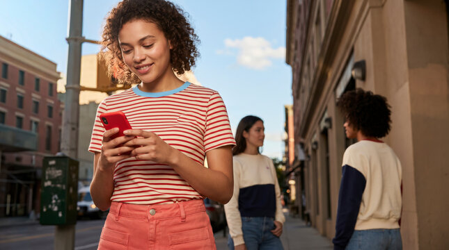 Young woman using smartphone in summer striped shirt on sunlit city street