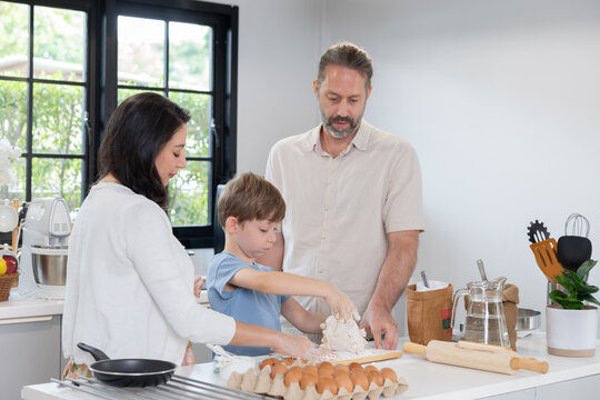 parent helps their young son mix flour in a bowl on the kitchen counter.