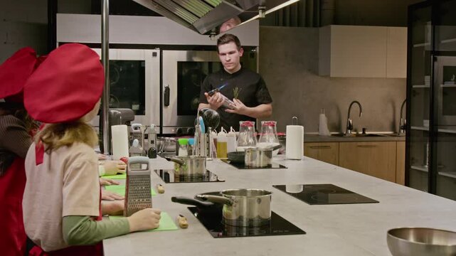 Caucasian young male chef lighting blowtorch during culinary class for Caucasian children. Video is perfect for promoting children culinary schools and educational workshops
