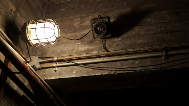 Industrial caged light fixture illuminating dark underground concrete tunnel