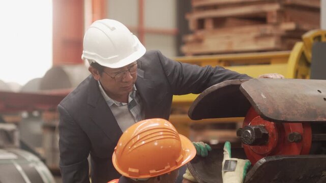 Close-up shot of an executive with a white safety helmet and a veteran technician inspecting steel components and machinery equipment. Demonstrating quality assurance, industrial maintenance, teamwork