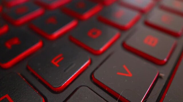 Detailed macro shot of a laptop keyboard featuring black keys with bright red illuminated lettering and red trim, suitable for technology and gaming themes, Uk