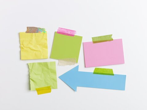 A photo of four overlapping paper notes of varied shapes (square, rectangle, arrow), colors (yellow, green, pink, blue), and textures (crumpled, smooth, torn), attached with different washi tapes