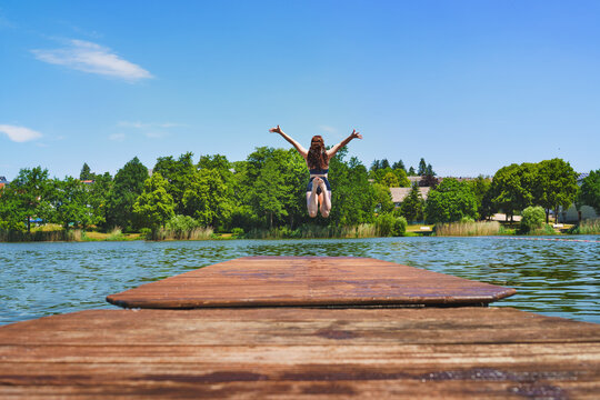 A shot of an attractive young woman in a bikini at a small lake. She is jumping into the water from a wooden jetty. "Jumping into vacation" concept.