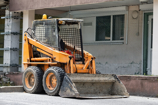 A construction vehicle is parked next to a building on a city street. It is ready for work in a construction or renovation project