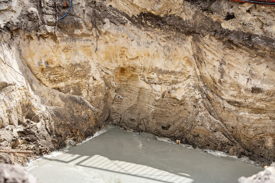 Workers are preparing concrete in a pit for the construction of a foundation at a construction site in an urban area during daylight hours