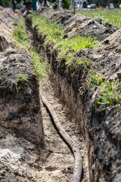 Workers are laying a high voltage cable in a trench at a construction site, with dirt and grass along the edges and bright daylight present