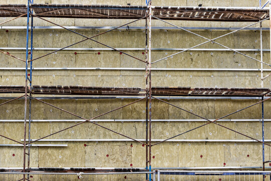 Workers are using mineral wool to insulate the fa&ccedil;ade of a building while on scaffolding. The activity takes place in a busy urban area during daylight hours