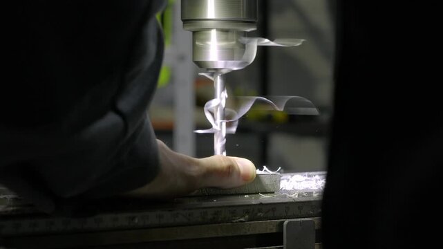 Close-up of a human male hand while working in a production workshop. The process of drilling holes in metal - metal shavings fly in different directions.