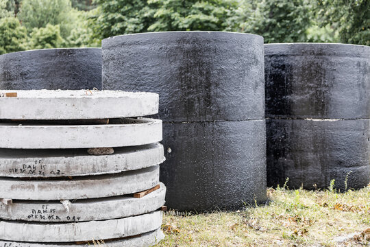 Workers place round black and gray concrete structures in a grassy area. The scene shows trees and an overcast sky. Tools are scattered nearby as work continues