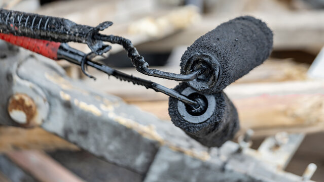 Workers use rollers to coat surfaces with bitumen mastic for waterproofing foundations at a construction site. The process occurs in bright daylight