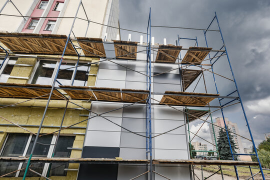 Workers install mineral wool insulation on the facade of a building while using scaffolding. This activity takes place in a busy urban setting under cloudy skies