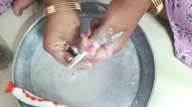 Woman cleaning dirty silver bangles with toothbrush and paste at home, close-up