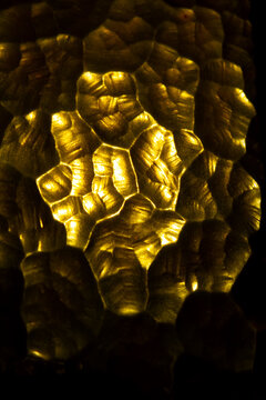 Golden glass pattern top view. Abstract mosaic texture macro. Amber backlit surface wallpaper. Luxury material backdrop. Bumpy cellular layout. Metallic yellow reflection close up. Glowing