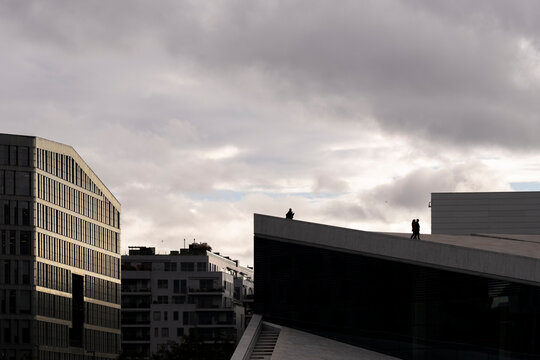 Dark clouds gather above modern office buildings as dramatic light and angular rooftops shape a moody urban architecture scene