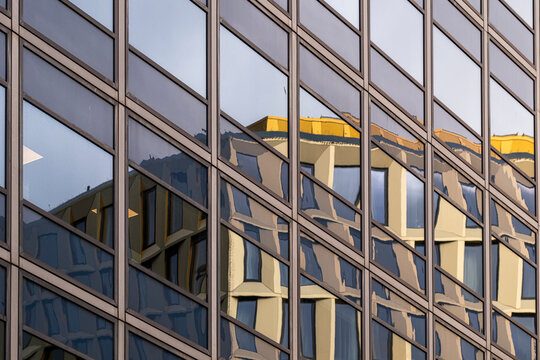 Reflective glass facade mirrors nearby buildings as repeating windows and angular forms create an abstract urban architecture pattern