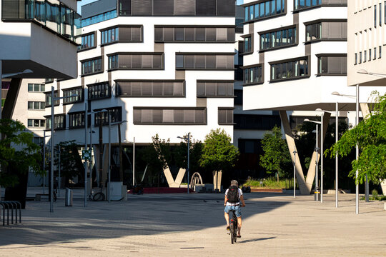 A cyclist crosses an open plaza beneath modern architecture as white apartment blocks and urban design shape the contemporary public space