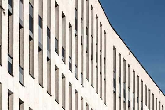 Minimalist concrete facade rises in geometric perspective as narrow windows repeat across modern architecture beneath a deep blue sky