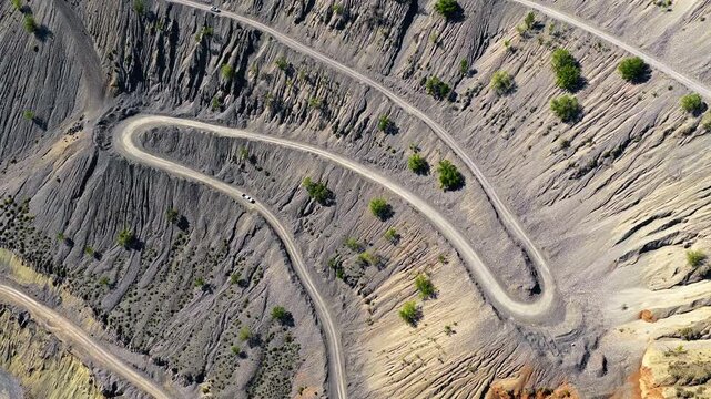 Aerial view of winding dirt roads curving through steep, eroded canyon slopes in Xinjiang, China.