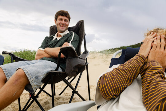 UGC Man laughing in beach chair beside friend hiding face