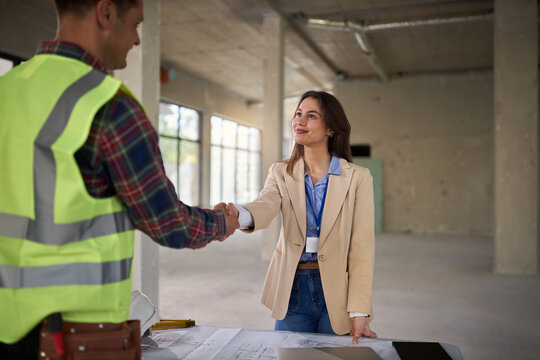 Young female architect and a manual worker reaching an agreement at a building site.
