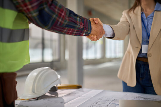 Close up of a male manual worker and a female building contractor shaking hands after coming to an agreement at a construction site