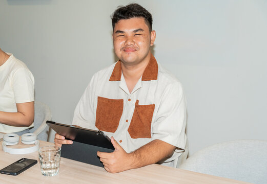 Young Asian Man Sitting at Table Using Tablet in Indoor Setting