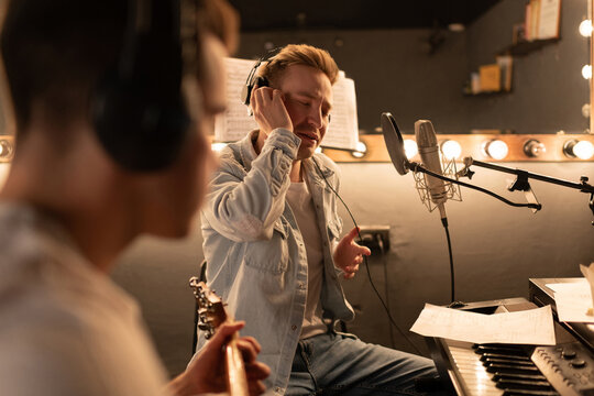 Male vocalist creating song with guitarist in sound studio