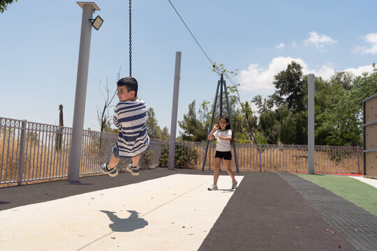 Boy Flying On Zip Line With Girl Watching In A Sunny Playground