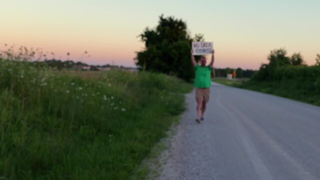 Middle-aged man holding handmade No Data Centers placard peaceful protest in Midwestern United Stated rural field near industrial area