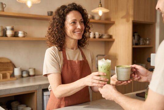 Smiling barista handing two matcha drinks to a customer across the counter