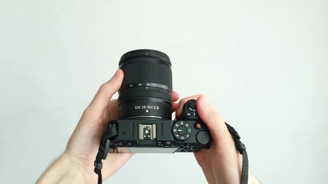 Professional photographer hand holds modern black camera with lens against clean background.