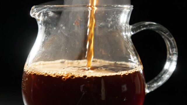 Coffee glass pitcher pour beverage brown liquid drink refreshment transparent stream filling clear carafe with foam bubble detail on dark background cafe brewing close up hot caffeine scene