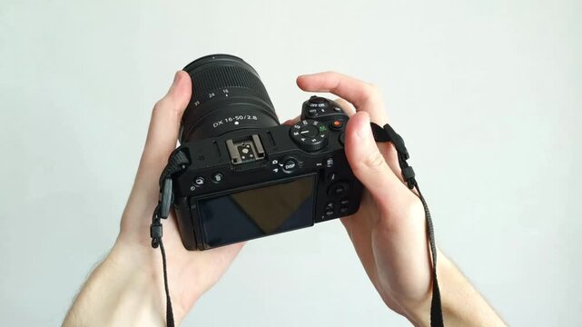 Professional photographer hand holds modern black camera with lens against clean background.