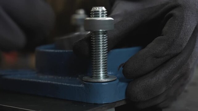 A worker tightens a nut onto a bolt, attaching an engine to a metal base.